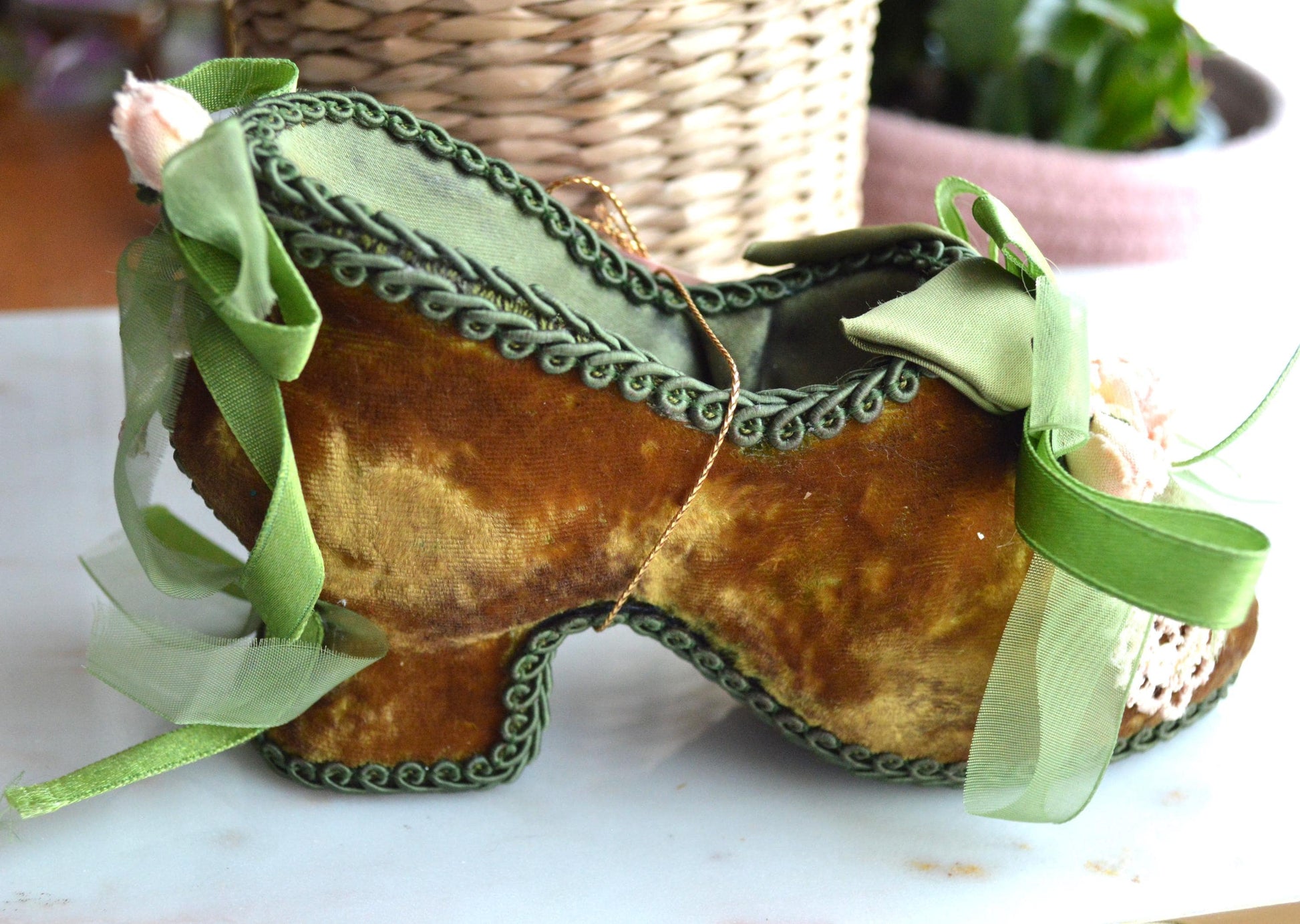 May include: A decorative shoe-shaped container in a vintage style. The shoe is made of brown velvet with green trim and ribbons. It features a high heel and is adorned with small flowers and lace.